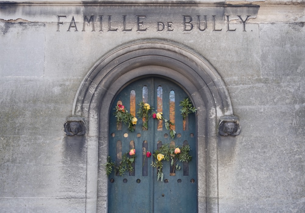 Flowers on the front of a stone mausoleum with an engraved sign for “Famille de Bully